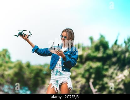 Carina ragazza controlla il drone con il telecomando. Drone volante all'esterno in estate Foto Stock