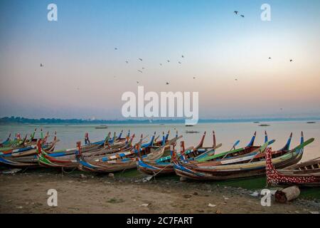 Barche a remi colorate allineate lungo la riva del lago Taungthaman ad Amarapura, Myanmar Foto Stock