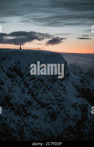 Scatto verticale del sole che tramonta sulle affascinanti montagne innevate a Nordkapp, Norvegia Foto Stock