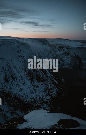 Scatto verticale del sole che tramonta sulle affascinanti montagne innevate a Nordkapp, Norvegia Foto Stock