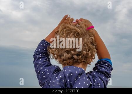 Bellissimi capelli ricci di ragazzino che si alza le mani davanti al cielo. Concetto di cura dei capelli Foto Stock