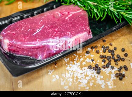 Bistecca di manzo in confezionamento sottovuoto e spezie su tagliere di legno Foto Stock