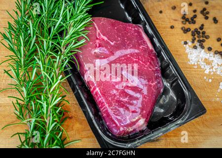 Bistecca di manzo in confezionamento sottovuoto e spezie su tagliere di legno Foto Stock