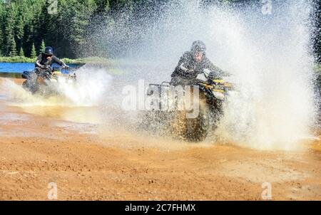 Due uomini che guidano il quad ATV attraverso il fiume spruzzi d'acqua lago ad alta velocità. Foy, lago Foyross, Sudbury, Canada. Foto Stock