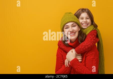 Ritratto invernale di famiglia felice e amorevole con cappelli, snodi e pullover in maglia. Madre e bambina che si divertono, giocano e ride su giallo bac Foto Stock