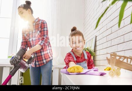 La famiglia è felice di pulire la camera. Madre e figlia fanno la pulizia in casa. Una giovane donna e una bambina spazzarono la polvere e aspirarono il Foto Stock