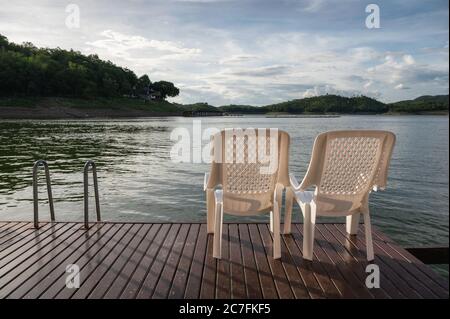 Due sedie di plastica sul ponte che galleggia in lago alla sera Foto Stock