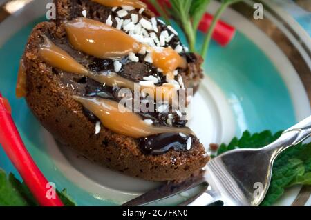 Un pezzo di torta al cioccolato morso e caramelle di gelatina colorate su un piatto decorato con menta, scaglie di cocco e latte condensato primo piano Foto Stock