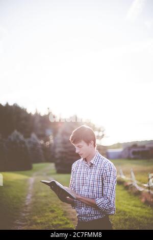 Maschio bianco che indossa una camicia di flanella che legge la bibbia sotto i raggi luminosi del sole Foto Stock