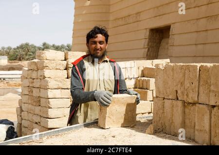 Raghba, Arabia Saudita, febbraio 16 2020: Un operaio di costruzioni musulmano in Arabia Saudita scarica mattoni di fango da un camion. Foto Stock