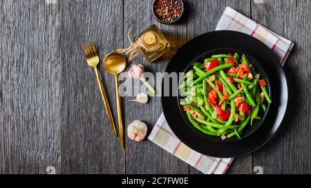 Primo piano di fagioli di cortile con cipolle e pomodori, Fry bodi in una ciotola nera su un tavolo di legno con posate dorate, vista panoramica dall'alto, f Foto Stock