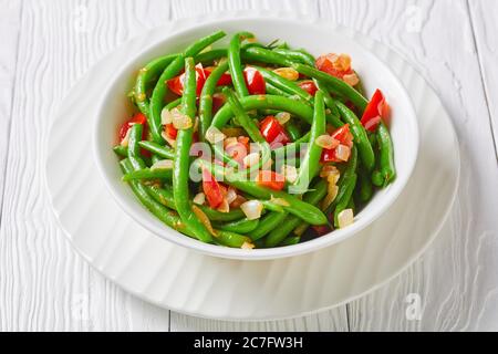 Primo piano di fagioli verdi con cipolle e pomodori, Fry bodi in una ciotola bianca su un tavolo di legno, vista panoramica dall'alto Foto Stock