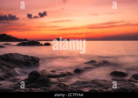 Tramonto su la pietra, la roccia rossa dell'Ile Rousse, nella regione Balagne della Corsica con onde mediterranee che si infrangono sulla costa rocciosa del Foto Stock