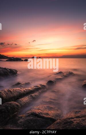 Tramonto su la pietra, la roccia rossa dell'Ile Rousse, nella regione Balagne della Corsica con onde mediterranee che si infrangono sulla costa rocciosa del Foto Stock