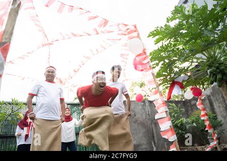 Tre giovani si sono Uniti felicemente nella corsa del sacco saltando rapidamente per raggiungere il traguardo nella celebrazione del 17 agosto indonesiano Independence Day Foto Stock