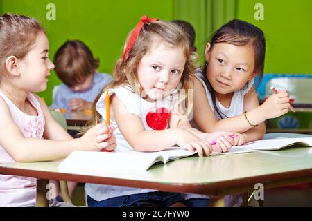 Tre ragazze felici dipingono insieme con matite in asilo Foto Stock