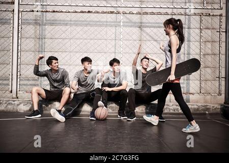 giovane donna asiatica adulta skateboarder dando un gruppo di giovani uomini hi-cinque Foto Stock