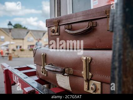 Vista ravvicinata e poco profonda delle valigie in stile vintage caricate su un trolly del periodo del vapore situato in una stazione ferroviaria britannica del periodo. Foto Stock