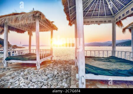 Tettoie e tende dal tetto di paglia sulla spiaggia Copacabana al tramonto a Dubrovnik. Ubicazione: Dubrovnik, Dalmazia, Croazia, Europa Foto Stock