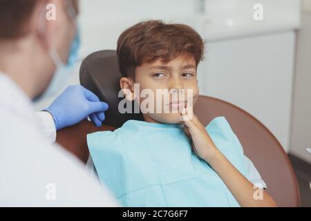 Ragazzo giovane che ha mal di denti, seduto in una sedia dentale durante l'esame dentale. Un dentista professionista che si prepara a curare i denti di una y Foto Stock