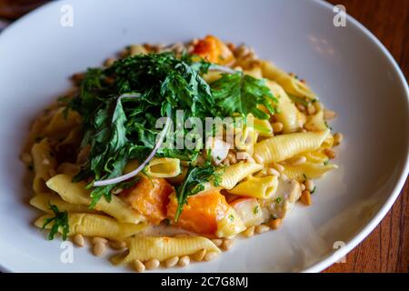 Pasto delizioso con patate dolci, pasta, pollo e verdure in un piatto bianco Foto Stock