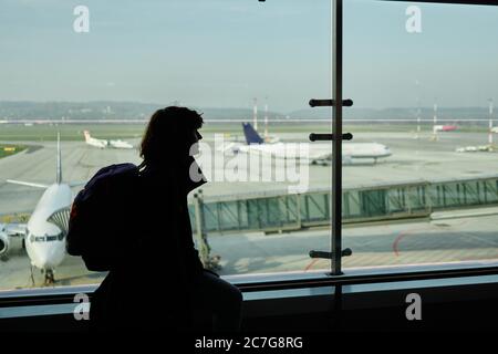 Donna viaggiatore con zaino in piedi vicino alla finestra di vetro dell'aeroporto su offuscata vista aereo dalla lounge nel terminal dell'aeroporto contro il cielo. Silhouette o Foto Stock