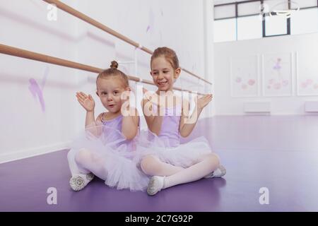 Foto a lunghezza intera di due graziose ballerine che giocano a peekaboo alla scuola di balletto, spazio di copia. Felici ragazze adorabili in leotards e tutu gonne Foto Stock