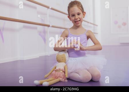 Bella giovane ballerina ragazza sorridente, mostrando segno di cuore con le mani, copia spazio. Adorabile ballerina ragazza che le tiene le mani in forma di cuore. L Foto Stock