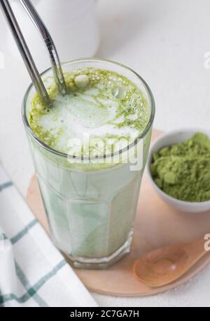 Fuoco selettivo, tè caldo matcha, latte, in vetro ad alta trasparenza e tubi metallici, con latte, in un interno domestico con piatti bianchi Foto Stock