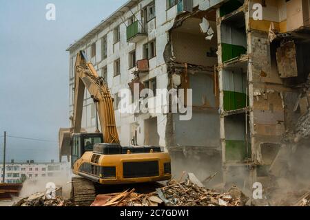 Demolizione di una storia di cinque in appartamento edificio riconosciuto come alloggiamento di emergenza, close-up di un escavatore benna raccoglie rifiuti di costruzione Foto Stock