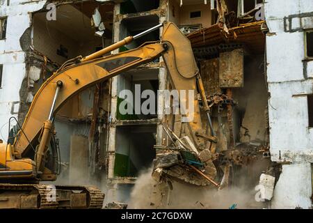 Demolizione di una storia di cinque in appartamento edificio riconosciuto come alloggiamento di emergenza, close-up di un escavatore benna raccoglie rifiuti di costruzione Foto Stock