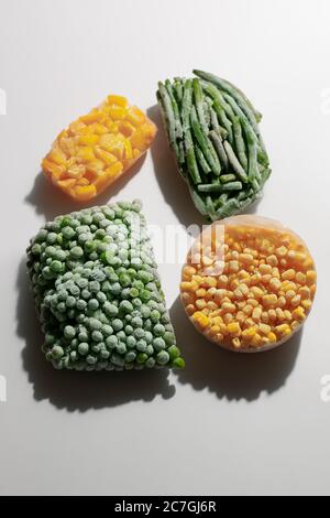 Astratto composizione moderna di verdure surgelate, mais, pepe, piselli verdi e fagioli su sfondo bianco con ombra. Concetto di alimentazione sana Foto Stock