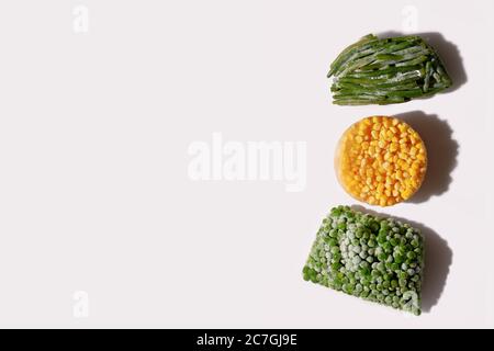 Composizione moderna astratta di mais, piselli verdi e fagioli surgelati su sfondo bianco con spazio di copia. Concetto di alimentazione sana Foto Stock