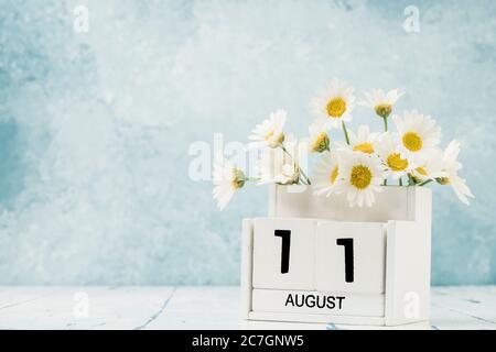 Calendario cubo bianco per agosto decorato con fiori margherita su blu con spazio copia Foto Stock