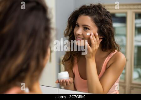 Bella donna di applicare una crema idratante sulla sua faccia. Foto Stock