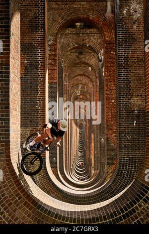 Joe Bowers guida la sua BMX bike mentre la gente goda una giornata fuori al Viadotto della Valle di Ouse a Balcombe, Sussex occidentale. Foto Stock