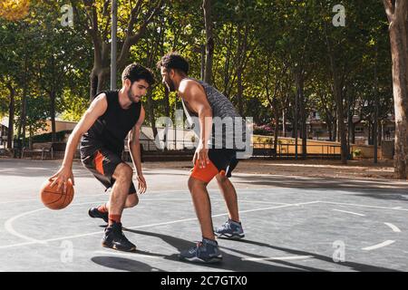 due giovani uomini che giocano a basket all'aperto lottano per la palla Foto Stock