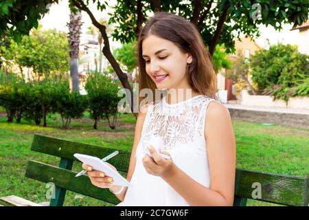 Ragazza carina è in possesso di una penna e un blocco note e carta sgualcita seduta sul banco di lavoro esterno. Foto Stock