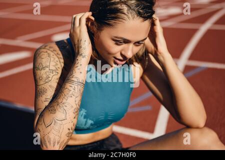 Primo piano bella atleta bagnata ragazza in abbigliamento sportivo pensieroso riposarsi dopo l'allenamento allo stadio Foto Stock