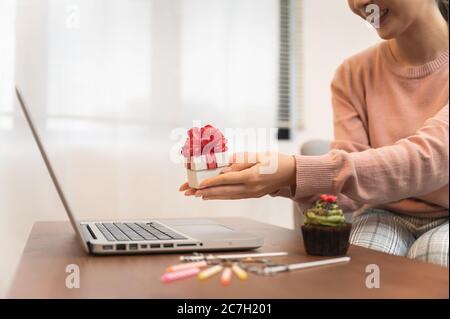 Donna asiatica che festeggia il compleanno di un collega con la videochiamata online che tiene giftbox a portata di mano mentre è isolata rimanere a casa Foto Stock