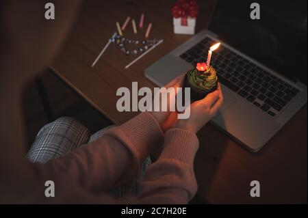 Donna asiatica che festeggia il compleanno di un collega con una videochiamata virtuale a casa mentre è isolata, resta a casa. Torta della tazza con la mano si accende Foto Stock