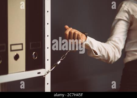 Donna d'affari bloccata in ufficio. Donna mano ammanettato a libreria ufficio con cartelle. Concetto di blocco. Primo piano. Immagine colorata Foto Stock