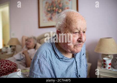 Una coppia anziana negli anni 80 si sedette sul letto nei pigiami prima di alzarsi al mattino, in Inghilterra, Regno Unito Foto Stock