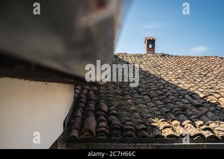 Vecchio tetto arrugginito coperto di mossi sotto la luce del sole e un cielo blu Foto Stock