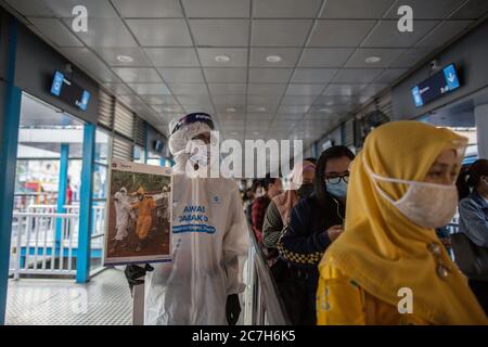 Giacarta, Giacarta, Indonesia. 17 luglio 2020. Un dipendente che indossa un equipaggiamento protettivo come precauzione contro il nuovo coronavirus ha un banner che mostra informazioni sul virus e su quelli infetti presso la stazione centrale di Harmoni a Giacarta, Indonesia, il 17 luglio 2020. Secondo il funzionario del ministero della sanità, i casi COVID-19 in Indonesia sono saliti di 1,462 in un giorno a 83,130, con il numero di morti che si è aggiunto di 84 a 3,957. Nelle ultime 24 ore, nove province hanno registrato un numero elevato di casi. Credit: Afriadi Hikmal/ZUMA Wire/Alamy Live News Foto Stock