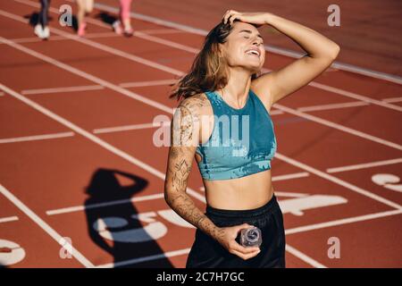 Allegra atleta bagnata in abbigliamento sportivo che riposa felicemente dopo aver corso sullo stadio Foto Stock