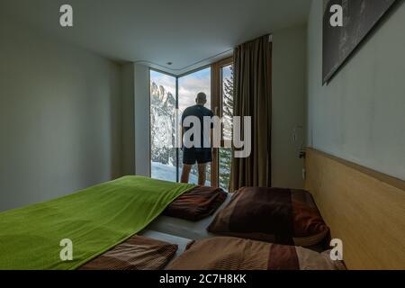 Europa, Austria, Tirolo, Tirolo Orientale, Lienz, l'uomo si affaccia sulla finestra panoramica della sua stanza sulla Dolomitenhütte Foto Stock