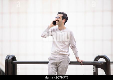 giovane uomo dirigente sorridente accanto agli uffici che parlano al telefono Foto Stock