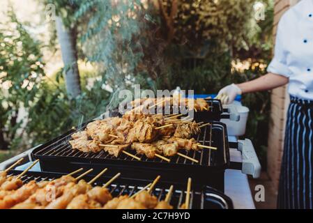 Spiedini di pollo cucinati su un barbecue da un ristoratore a una festa Foto Stock