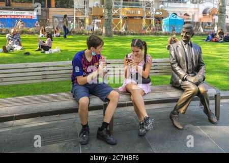 Londra, Regno Unito. 17 luglio 2020. La gente gode di un rinfresco accanto alla statua del sig. Bean in Leicester Square. Il West End sta lentamente diventando più affollato mentre la gente torna a negozi e parchi nel centro di Londra sotto il sole. Credit: Imageplotter/Alamy Live News Foto Stock